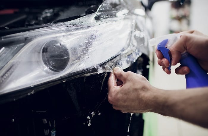 Worker hands installs car paint protection film wrap auto headlight