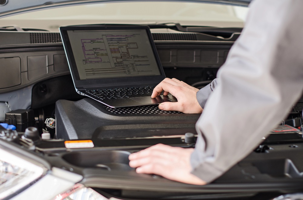 Mechanic with laptop diagnoses car in workshop